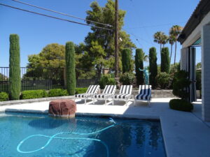 Backyard pool with lounge chairs and statue under blue sky.