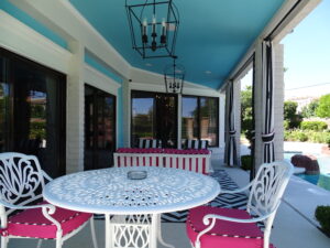 Stylish patio with turquoise ceiling and pink chairs.