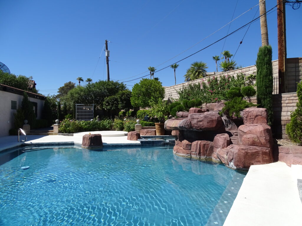 Sunny backyard pool with artificial rock formation and plants