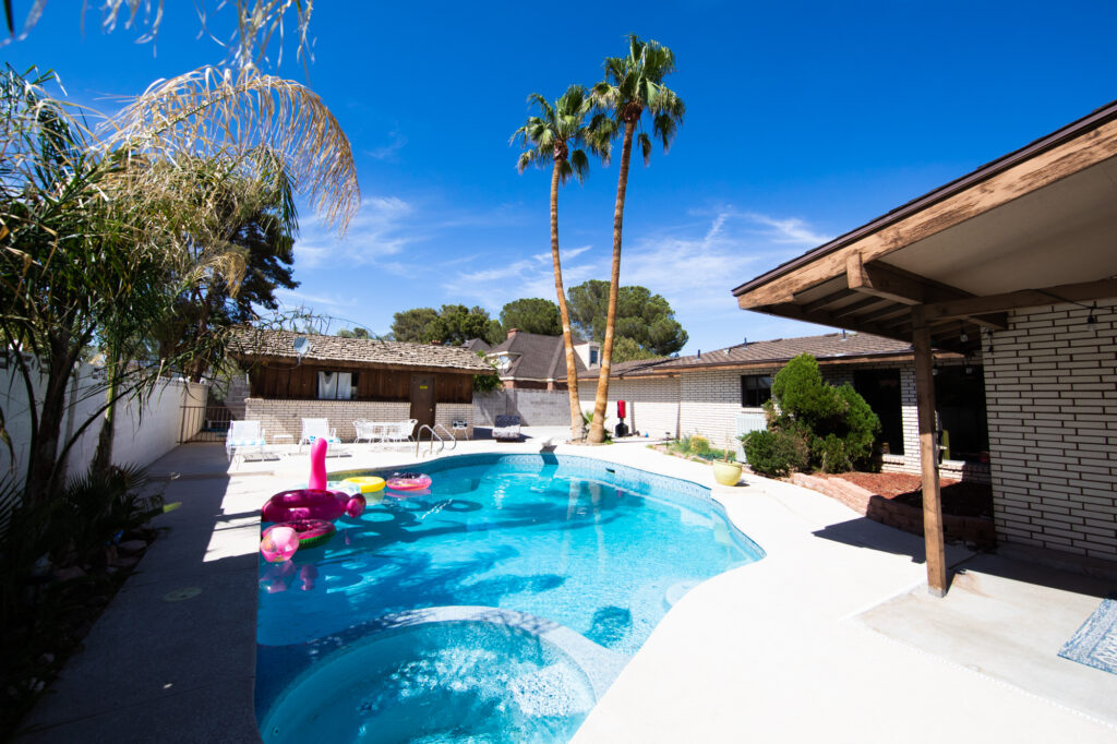 Sunlit backyard with pool, palm trees, and colorful floaties