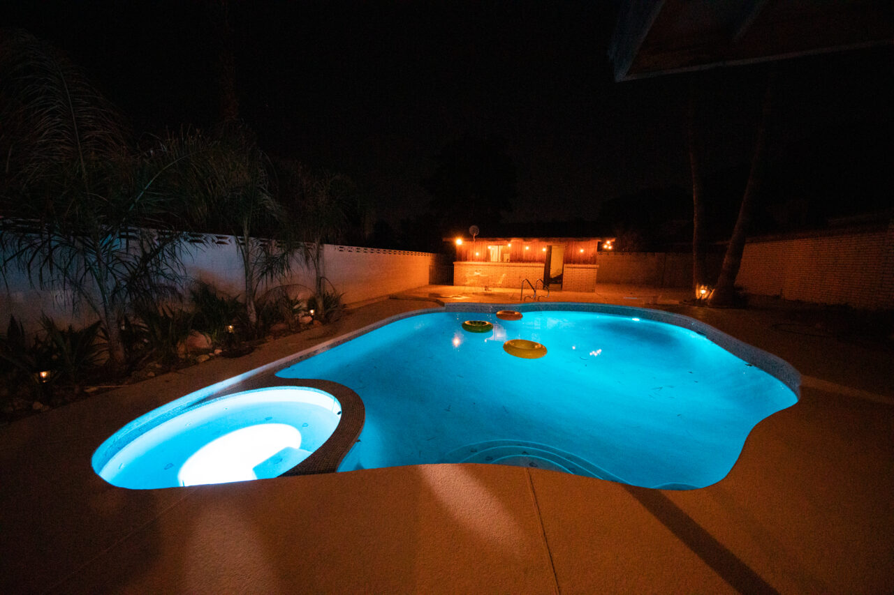 Illuminated backyard pool at night with floating rings